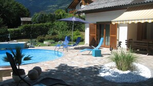 A pool area with lounge chairs, a small pool, and a garden with plants and a decorative rock arrangement. - Erna Angermaier by Interhome (Flattach)