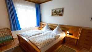 A neatly arranged bedroom with a wooden bed, a crib, and a painting on the wall. - Erna Angermaier by Interhome (Flattach)