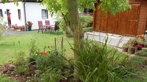 Un jardin bien entretenu, agrémenté de diverses plantes et fleurs, une porte en bois et un bâtiment blanc avec une chaise rouge à l’extérieur.