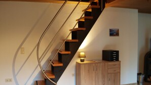 Un escalier en colimaçon avec des marches en bois et des rampes en métal, menant à l’étage supérieur.