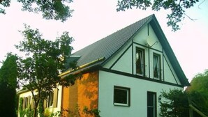Une maison à deux étages, dotée d’un toit à forte pente, de murs extérieurs blancs et d’une partie en briques sur le côté.