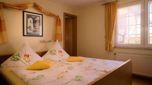 A bedroom with a bed, floral bedding, a framed picture on the wall, and a window with curtains. - FEWO Hortensie by Interhome (Bruttig-Fankel)