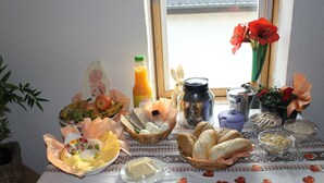 Ein Esstisch mit verschiedenen Speisen, einer Orangensaftflasche, einem Thermosbehälter und einer Vase mit Blumen.