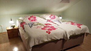 Ein Doppelbett mit floralem Bettbezug, ein Nachttisch mit Lampe und ein Beistelltisch mit Pflanze.