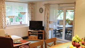 Una sala de estar con televisor, una mesa de comedor con fruta y vistas al exterior.