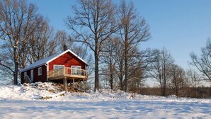 Eine rote Holzhütte mit einem Balkon, umgeben von verschneitem Gelände und kahl stehenden Bäumen.
