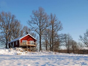 A red cabin with a balcony, surrounded by snow-covered ground and leafless trees. - Ekkulle by Interhome (Skillingaryd)