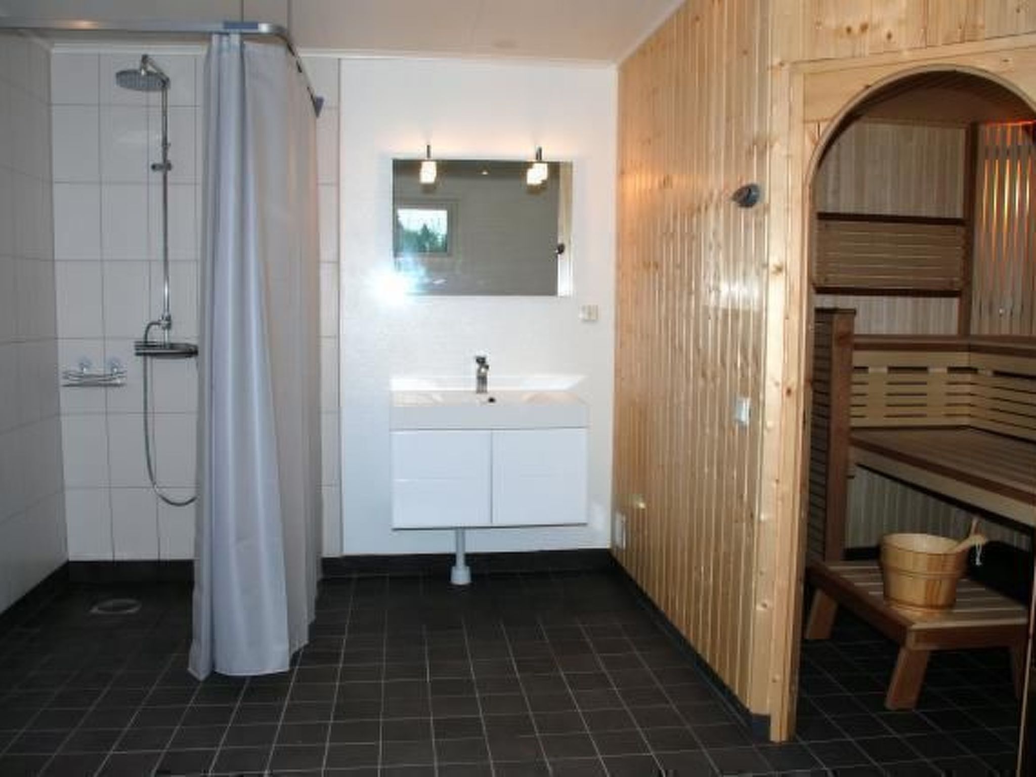 Un baño moderno con ducha, lavamanos y zona de sauna de madera.