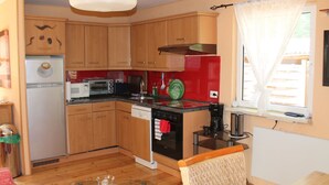 Una cucina compatta con mobili in legno, un frigorifero, un forno a microonde, una macchina per il caffè e una finestra con tende.