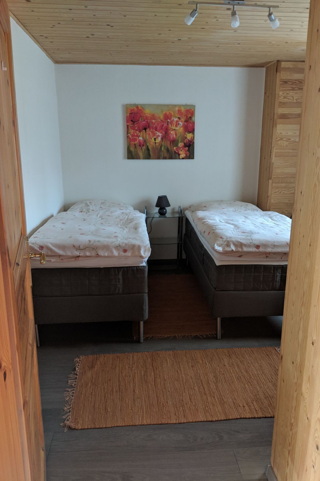 Une chambre avec deux lits, une table de chevet, une lampe et un tableau au mur.