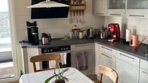 Een moderne keuken met witte kasten, een eettafel met stoelen en een hangende lamp.