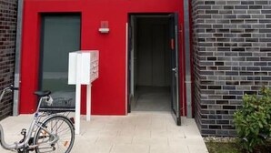 Een modern gebouw met een rode onderpartij, meerdere ramen en een fiets voor de deur.