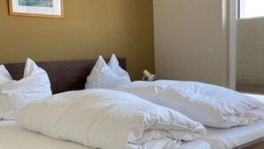 Een net opgemaakt bed met witte lakens en kussens, een houten hoofdbord en een lijst met een afbeelding aan de muur.