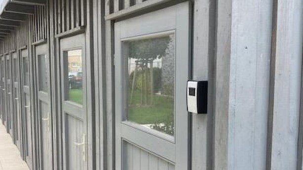Een rij grijze metalen deuren met ramen, een brievenbus en een deurklink.