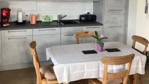 Een moderne keuken met grijze kastjes, een wit aanrechtblad en een eethoek met een tafel en stoelen.
