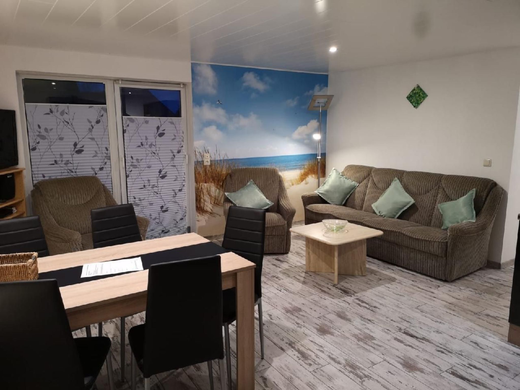 Una sala de estar con un mural de playa, un sofá, una mesa de centro y un comedor con sillas y una mesa.