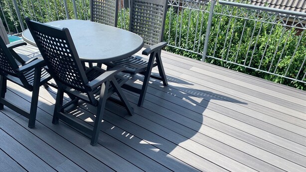 Eine Terrasse mit einem runden Tisch und Stühlen, umgeben von einem Metallzaun und Grünpflanzen.