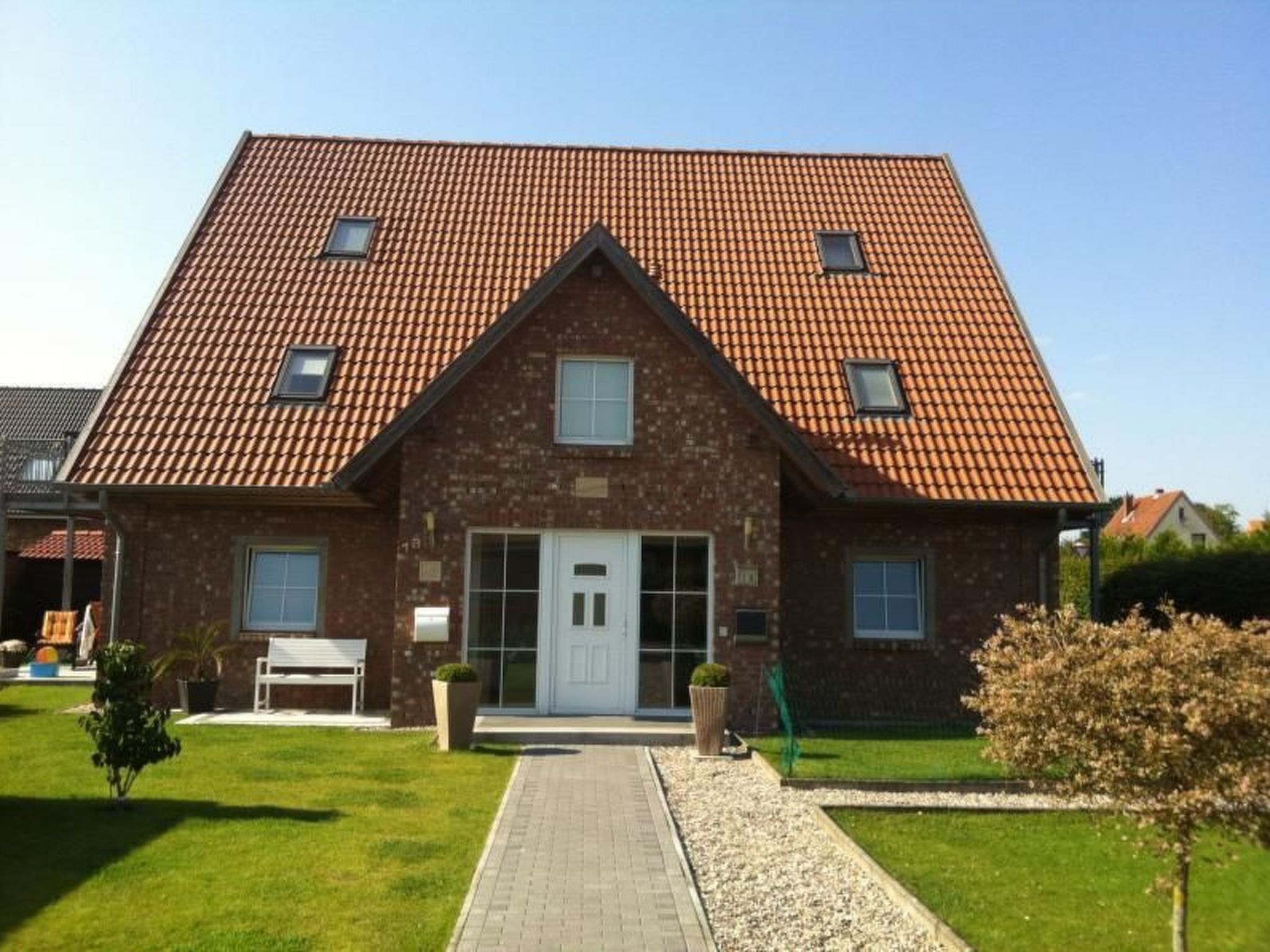 A two-story house with a red-tiled roof, a central entrance with a white door, and a small front garden.