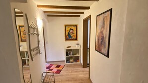A hallway with wooden flooring, a checkered rug, a metal rack, and a shelf with books and a small table. - Mayer in Oberkirch by Interhome (Oberkirch)