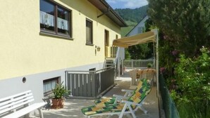 A yellow building with a patio area featuring a bench, two lounge chairs, and a potted plant. - Mayer in Oberkirch by Interhome (Oberkirch)