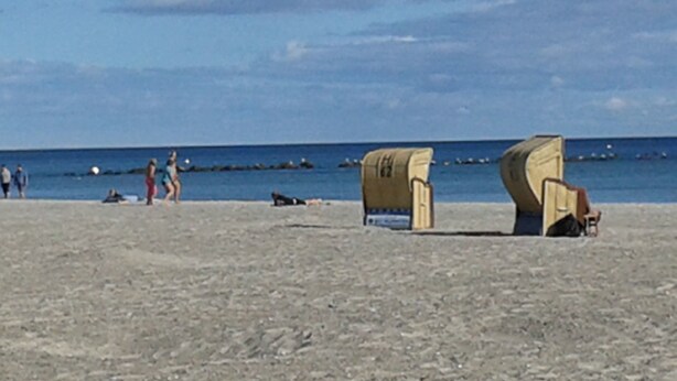 Een strand met enkele mensen, een houten constructie en de oceaan op de achtergrond.