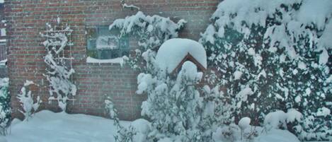 Un edificio de ladrillo con arbustos nevados y techo cubierto de nieve.