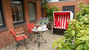 En patio med murstensvæg, et bord med stole, en rød-hvid stribet bænk og en potteplante.
