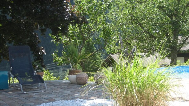 A patio area with a blue chair, a potted plant, and a small garden bed with white pebbles. - mit beheiztem Pool in Flattach by Interhome (Flattach)