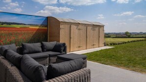 Un'area salotto esterna moderna con un divano in rattan e un capanno di legno.