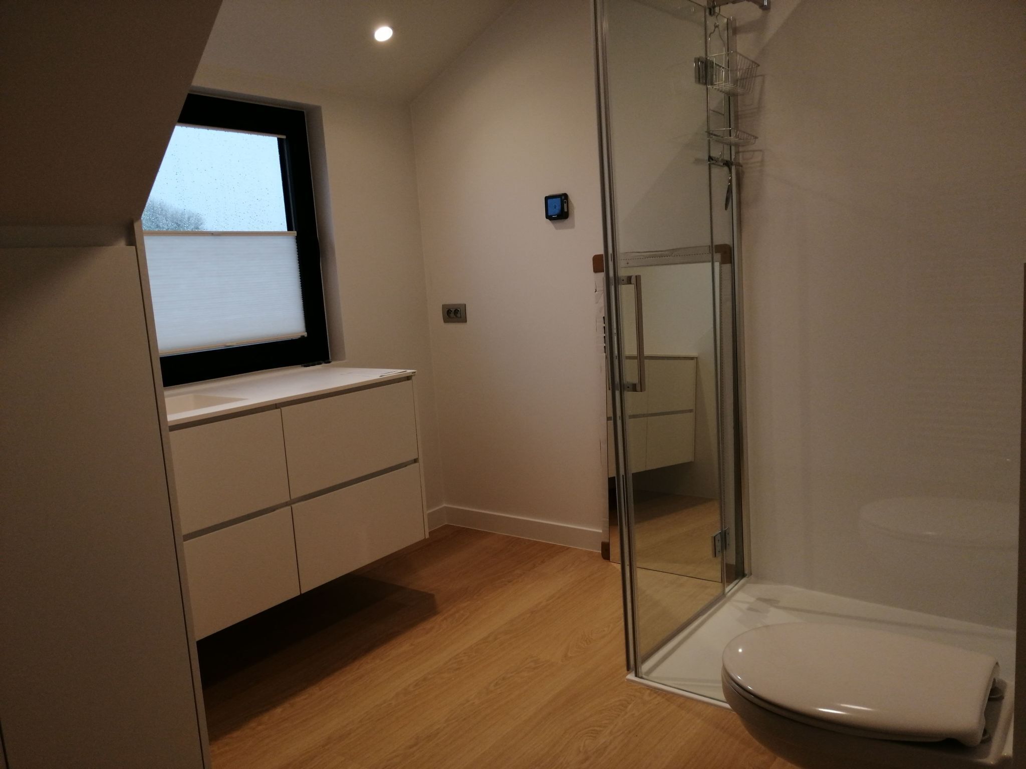 A modern bathroom with a glass shower enclosure, a toilet, and a built-in bench with storage.