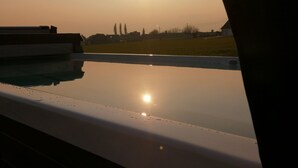 Vista dalla finestra su una piscina, con cielo sereno e il sole al tramonto.