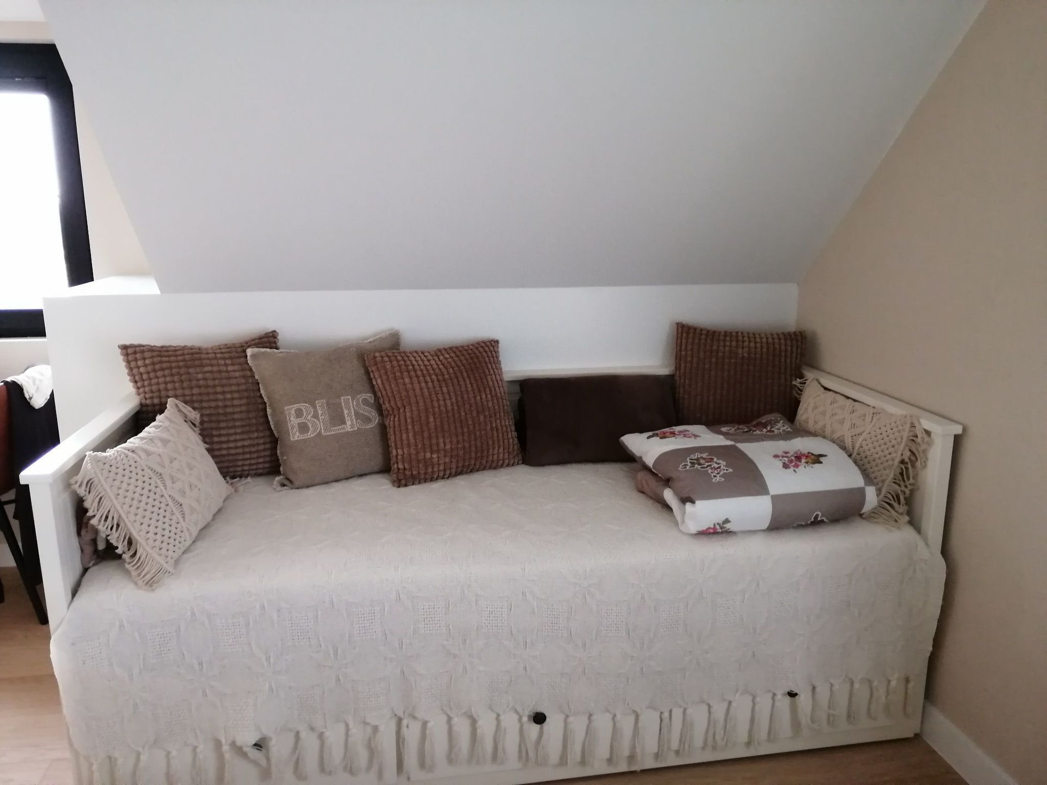 Een witte bank met een geribbelde hoes, meerdere kussens en een gebreide plaid.