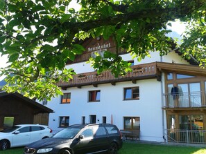 Ein Gebäude mit einem Schild, auf dem "Sonnenhof" steht. Vor dem Gebäude sind zwei Autos geparkt und es besitzt einen Balkon mit Geländer.