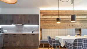 A modern kitchen with dark cabinets, a stainless steel countertop, and a wooden dining area with plaid chairs and a table. - Mont Blanc by Interhome (Sölden)