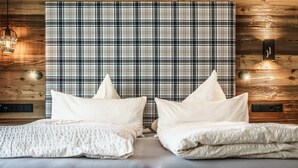 A bedroom with a plaid headboard, two white pillows, a textured blanket, and a wooden wall with a light fixture. - Mont Blanc by Interhome (Sölden)