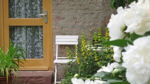 Una puerta con panel de vidrio, un banco blanco y flores amarillas en un jardín.