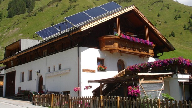 En traditionell chalet med ett sluttande tak, en träbalkong med blomlådor och solpaneler på taket.