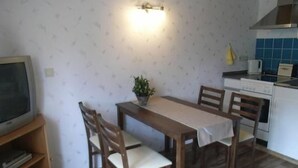 Una cocina compacta con una mesa de comedor, sillas, una pequeña planta en maceta y un televisor sobre un mueble de madera.