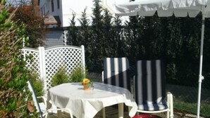 Un patio al aire libre con una mesa redonda, sillas blancas y un paraguas a rayas.