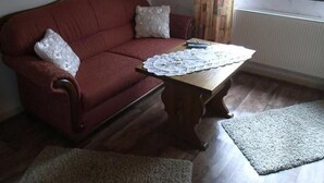 Una sala de estar con un sofá rojo, una mesa de centro de madera y dos cojines blancos.