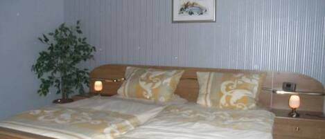 A bedroom with a bed, bedside tables, a lamp, a framed picture on the wall, and a potted plant.