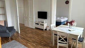 Ett modernt vardagsrum med en grå soffa, ett matbord med stolar, en TV och ett litet vitt skåp.