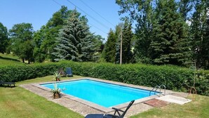 Piscina rectangular con superficie de agua azul cristalina, rodeada por un césped bien cuidado y setos verdes frondosos.