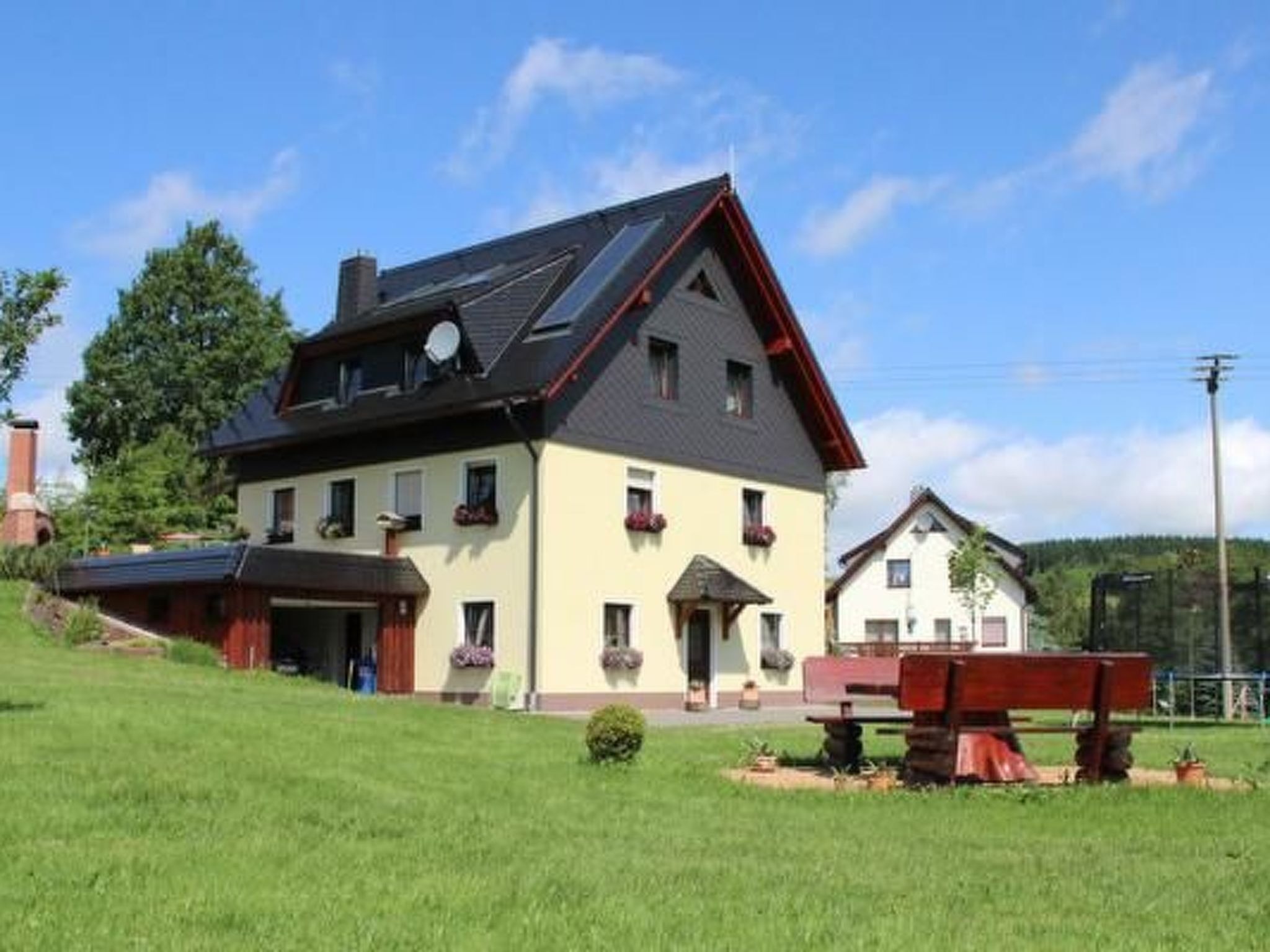 A two-story house with a sloped roof, a chimney, and a small garden with a bench.