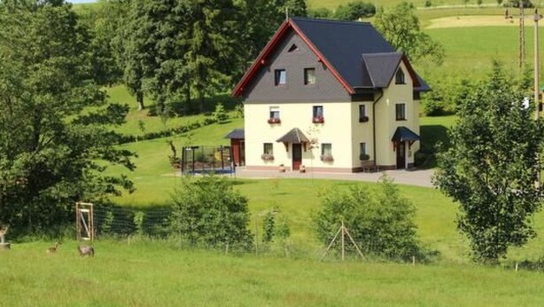 Una casa de dos pisos con techo rojo, rodeada de exuberante follaje y árboles.