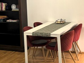 Un comedor con una mesa blanca, camino de mesa estampado y sillas tapizadas rojas.