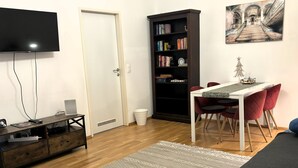 A living room with a flat-screen TV, a wooden cabinet, a dining table with red chairs, a bookshelf, and a painting on the wall. - Wohnen am Augarten by Interhome (Vienna)