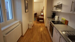 A narrow hallway leading to a dining area with a table and chairs, a radiator, and a kitchen with cabinets and appliances. - Wohnen am Augarten by Interhome (Vienna)