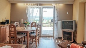 Ein Essbereich mit Holztisch und Stühlen, einem Fernseher und Blick ins Freie.
