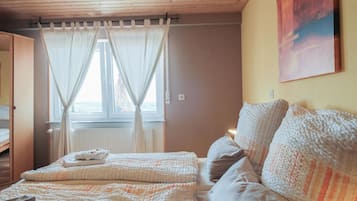 Un dormitorio con una cama, una ventana con cortinas, un radiador y un cuadro en la pared.